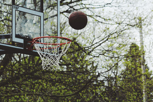 basketball almost going into hoop outside with trees in background